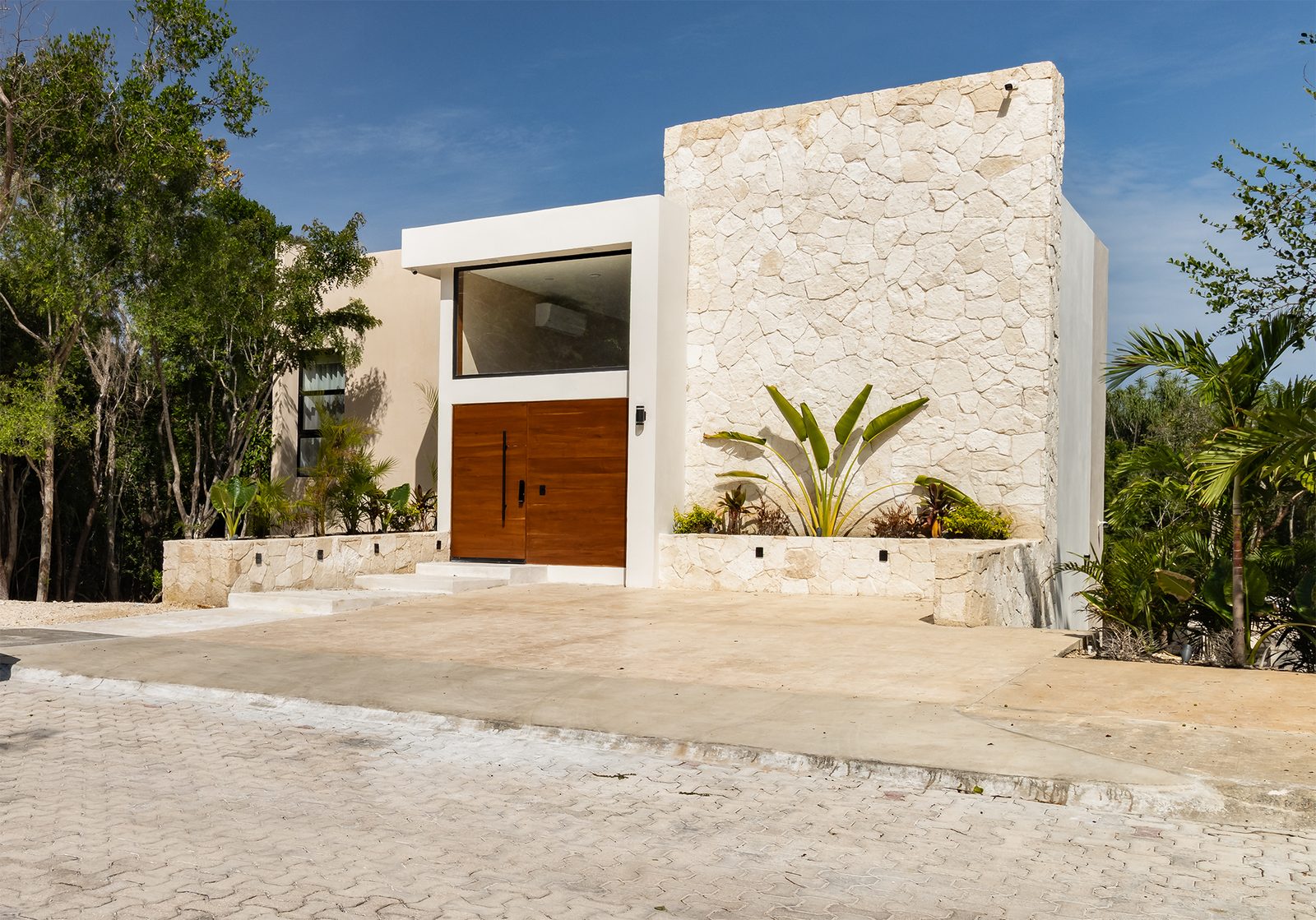 Stone-clad entry with oversized Tzalam wood door beneath a window of equal scale